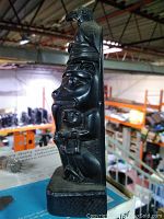 Side view of the dark soapstone carving showing detailed animal and humanoid figures carved vertically.