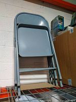 Photo shows stacked view of four steel folding chairs on a shelf, highlighting their solid steel seats and framed construction with rubber leg tips.