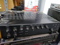 Front-left and top view of the black TOA 900 Series II Amplifier showing multiple rotary input level controls and switches on the front panel.