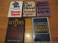 Five hardcover books laid out on a wooden floor, titles visible: three by Truman Capote, two related to Evelyn Waugh. All have dust jackets in good condition.