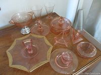Overview of all items in lot showing the candy box, glasses, creamer, footed bowl, tray with gold trim, small cup and saucer, and round dish.