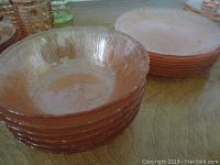 Stack of 6 pink depression glass bowls and stack of 8 matching plates placed on a table surface.