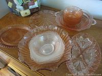 Overview photo showing various pink depression glass plates, bowls, and serving dishes arranged on a wooden surface.