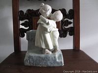 Front view of the porcelain figural vase showing two children embracing and the mottled blue vase base.