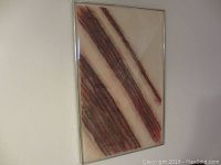 Framed abstract artwork showing diagonal reddish-brown fiber lines on a beige background, hung on a wall.