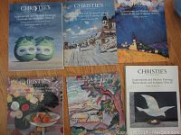 Five Christie's auction catalogues displayed flat showing varying covers including green apples, seaside, floral still life, and colorful impressionist art.
