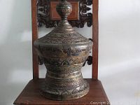 Front view of the antique Thai wooden container box sitting on a carved wooden chair showing overall shape and height.