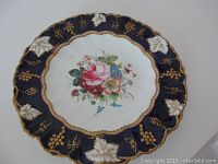 Top-down view showing the full front of the plate with central floral bouquet and cobalt blue border with gold grapevine detail.