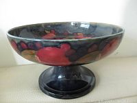 Side view showing the rich dark glaze and painted pomegranate design on the bowl and pedestal base.