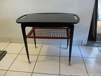 Front view of side table showing black lacquer tray top, red rattan shelf and brass caster wheels.