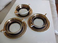 Overhead photo showing three Aynsley cream soup cups with matching saucers, highlighting cobalt blue and gold decorative pattern.