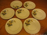 Seven Ridgway ironstone plates arranged on a wooden table, displaying floral pattern and ribbed edge detail.