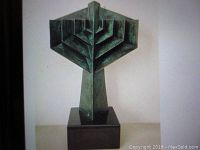 Front view of geometric cast bronze menorah sculpture with dark green patina on black marble base.