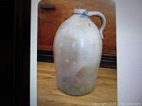 Front view of the entire jug on a wooden floor showing the light grey glaze and shape.