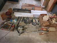 Full view of the tile cutting tools, marble thresholds, tile boxes, and drill laid out on the floor.
