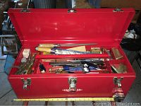 Photo of the red metal Craftsman toolbox opened to reveal a variety of unsorted hand tools including files, screwdrivers, and small tools inside divided compartments.
