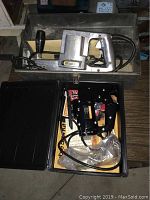 Top view showing Stanley Jab Saw with metal body and black handle alongside black Sabre Saw in case on floor.