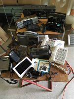 Overview of multiple electronics including radios, telephones, COBRA CB, battery charger, manuals on table