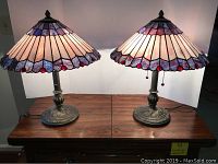 Front view of both lamps lit showing shades, red glass accent jewels, scalloped shade edges and ornate metal bases