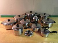 Overview of assorted Revere Ware pots and pans with lids arranged on a table.