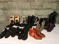 Full view of all footwear including new Timberland boots, ladies boots, and Totes rubber boot covers lined up on white cloth with brick wall background.