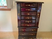 Front view of the cherry finish standing jewelry armoire showing multiple drawers and gold-colored hardware.