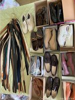 Photo showing the full lot of 11 pairs of men's shoes size 9.5 and a group of assorted belts laid out on cloth surface.