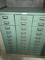 Front view showing 30 green metal drawers with metal handles and label holders.