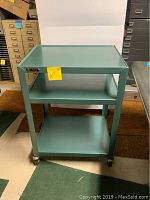 Front view of the green metal 3-tier rolling cart showing all three shelves and caster wheels.