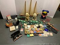 Group of vintage desk items on display including matchbooks, pocket knives, ceramic figurines, plush toy, and model sailboats.