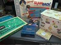 Photo showing several boxed card and tabletop games including Milton Bradley SlamBack Game box, Tudor Electric Football and Baseball Games, and other smaller boxed games on a table.