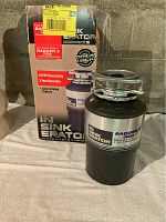 Food waste disposer unit with original box, showing InSinkErator branding and Badger 5 Plus model details.