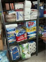 Full view of shelving unit with stacked packages of Charmin toilet paper (Ultra Soft, Ultra Strong, Mega Rolls), Bounty paper towels, and Marathon tissue pack.