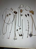 Full view of the assorted jewelry laid flat, showing various necklaces, earrings, bracelets, rings, and brooches on a white surface.