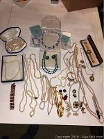 Full view of all jewelry pieces spread on white surface showing a diverse collection of gold-tone, pearl, lace agate, and cameo costume jewelry.