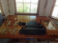 Full view of all lot items on wooden table showing pine clock, black shelf and various trivets and wall decor items
