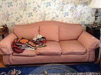 Front view of pink Ethan Allen sofa showing three cushions and fabric wear with items on seat cushions