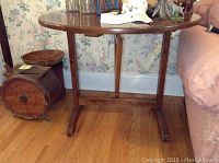 Round tilt top wooden table with pedestal base and three legs, showing the table top and floor beneath.