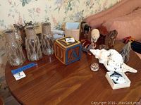 View of assorted animal figurines, three figurine bottles with burlap string accents, large seashells, and block bank on wooden table.