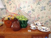 Photo showing hall pitcher, pottery bowls, faux fruit in ceramic leaf holder, and Wittembers china set with teacups, saucer, sugar pot, and tray on wooden surface.