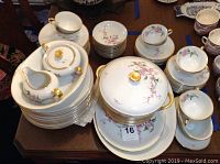 Photo showing various stacked porcelain items including covered sugar pot, creamer, saucers, cups, and plates with floral and gold design.