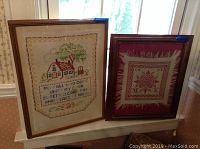 Three pieces of framed wall art resting on a window sill, showing two cross stitch pieces and one symmetrical stitch pattern in dark frame mats.
