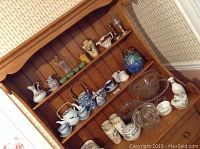 Wide view of multiple shelves holding teapots, creamers, teacups, pitchers, glass serving dishes, and decorative items.