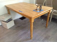 Full view of the wood kitchen table showing the tabletop and legs, with visible wear marks and adjacent items for scale.