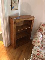 Pine bookcase with natural wood finish. Shows carved circular accents at upper corners and two internal shelves.