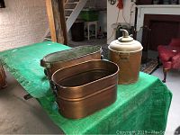 Two copper bins and iron water pump on green tarp in basement setting.