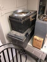 Two stacked black metal toolboxes, one with a coil of metal wire on top, next to a box of cabinet knobs and other tools.
