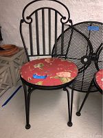Front view of one black metal chair with curved back and floral fabric seat cushion showing details of scrollwork on the back and cushion pattern.
