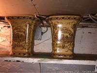 Two yellow porcelain plant containers side by side, each with brown decorative designs including birds and floral patterns, placed on a white shelf.