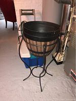 Tall black metal plant stand with a round faux wood planter container inside